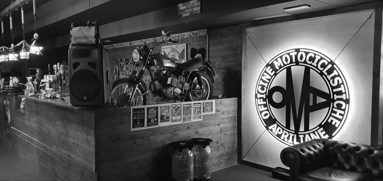 L'interno del locale: bancone in legno, moto esposte e il logo al neon